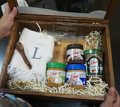 A wonderful gift for moms given by Lily's Peanut Butter : a customized bread box filled with Lily's Peanut Butter spread, with monogrammed table napkin, dessert spoon and wooden cutting board.